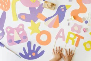 Creative art and craft layout with colorful paper cutouts and child’s hands, viewed from above.